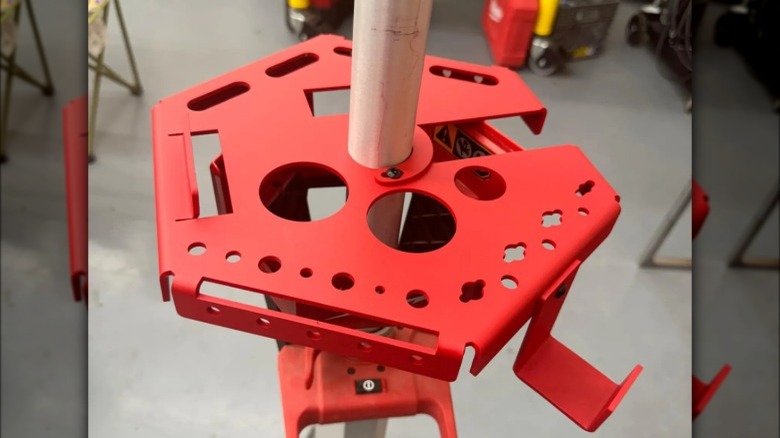 A close-up of a red aluminum tool rack mounted on a Milwaukee Rocket Light pole, showing multiple cutouts for tools and more.