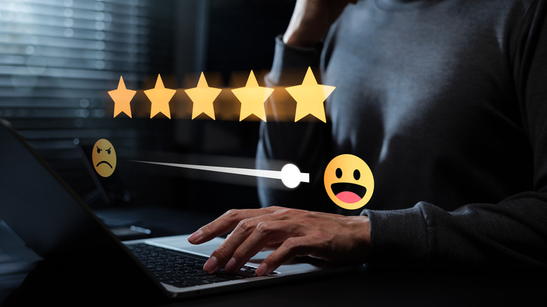 A person writing on a laptop. Flying five stars and a happy emoji represent a good review.