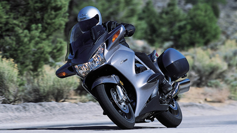 A rider leaning a Honda ST1300 ABS into a corner on a scenic mountain road.