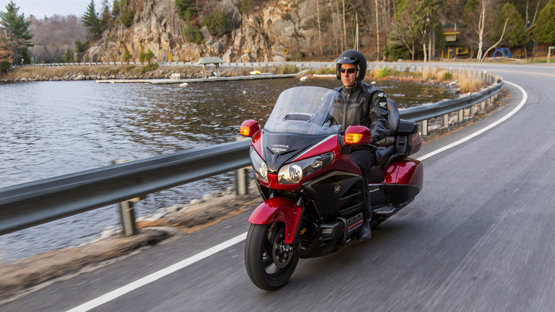 A rider cruising a red 2015 Honda Gold Wing GL1800 touring motorcycle along a lakeside road.