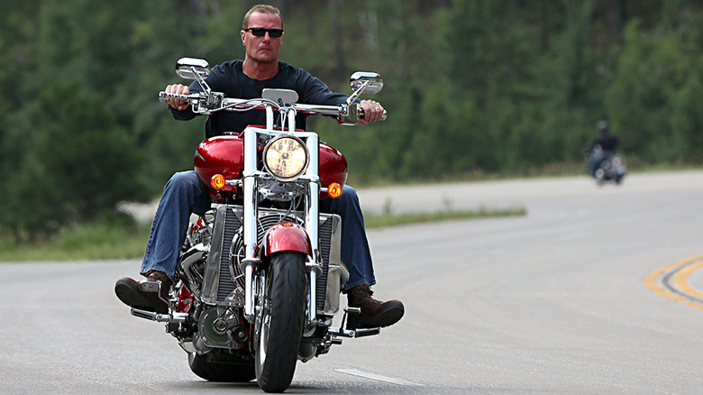 A man riding a large red Boss Hoss Classic Cruiser Bike on a winding road.