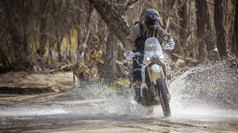 A motorcyclist riding a Kove 450 Rally adventure bike through shallow water.