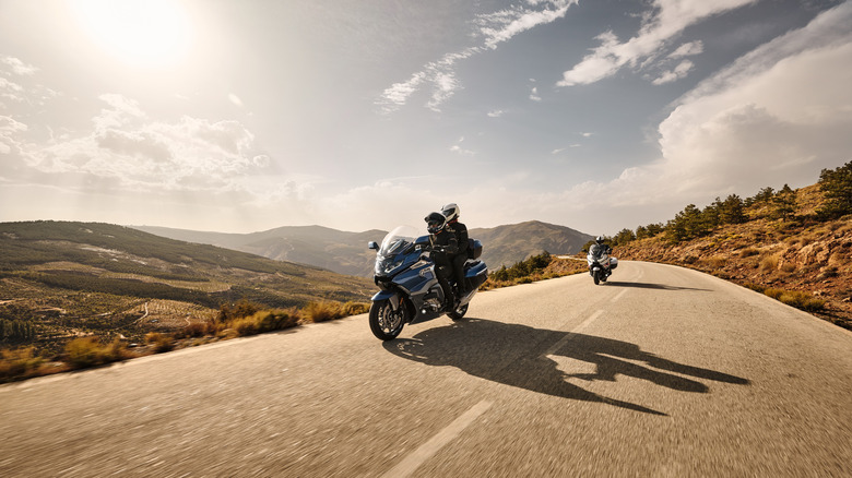 Two BMW K 1600 GTLs cruise along a sunlit mountain road.