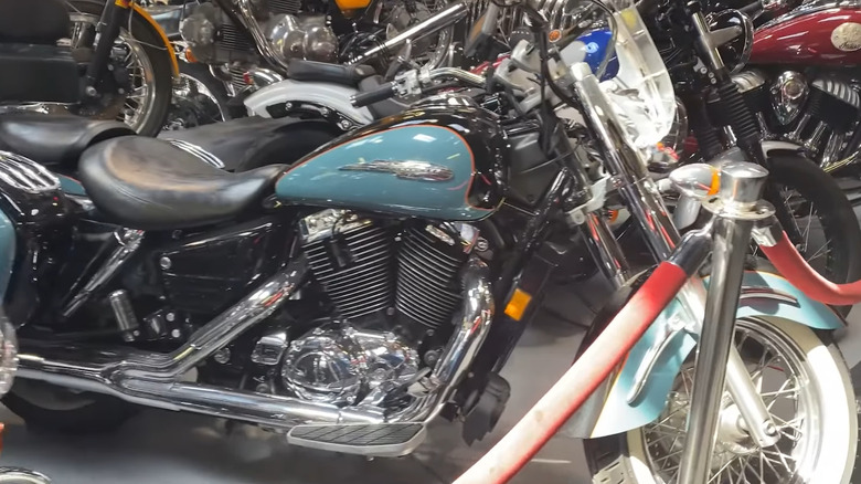 A light green-blue Honda Aero 1100 from 1999 parked alongside a row of other classic bikes