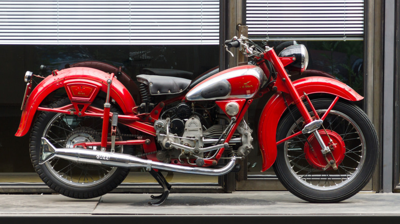 A red Moto Guzzi Airone with lots of chrome parked on its stand outside a store
