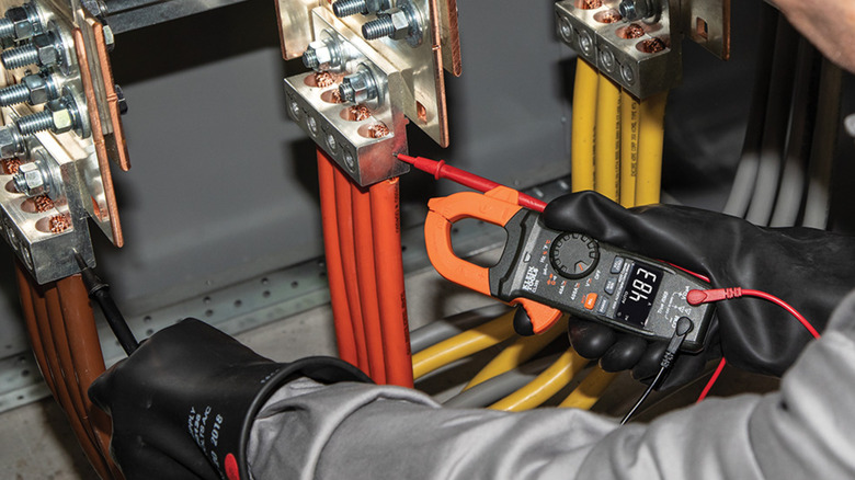 A Klein Tools clamp meter used by a professional on large cables.