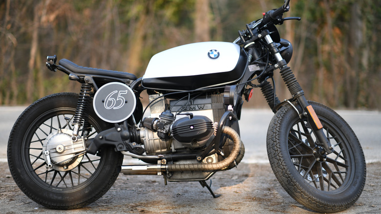 A white BMW caffe racer with elongated tank and exposed engine parked at the side of a street.