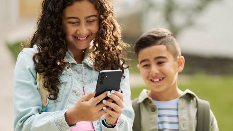 A kid holding a Bark phone while another kid looks on
