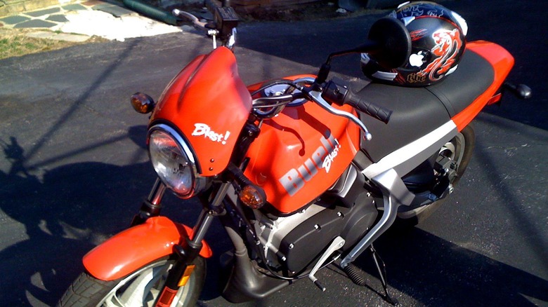 Orange Buell Blast with a helmet on the seating, resting on the pavement under the sunlight