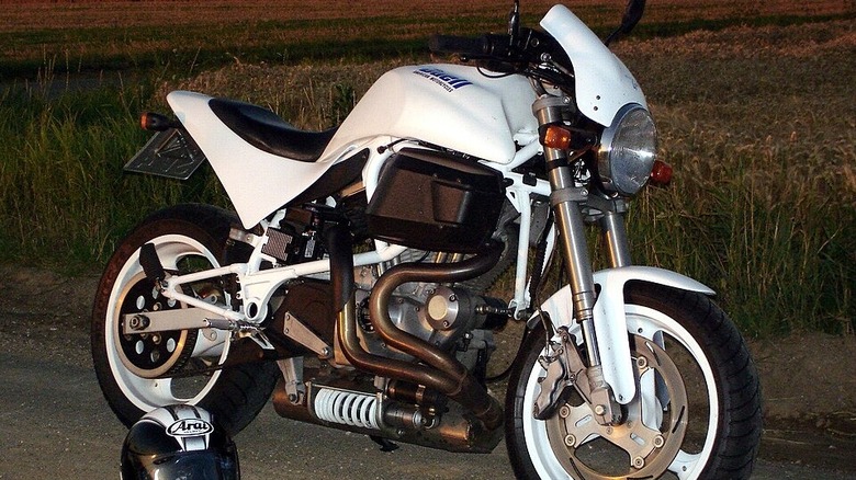 A white Buell S1 Lightning sitting in front of a field, with a sunset to its left side