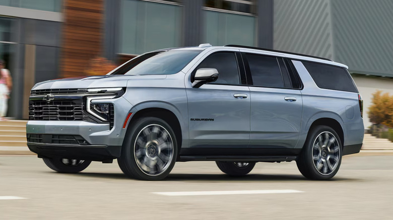 A gray Chevrolet Suburban driving down a town road.