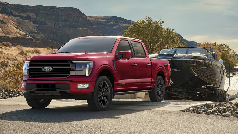 A red Ford F-150 towing a boat near a lake.