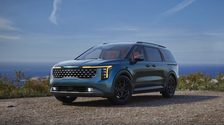 A blue Kia Carnival parked by a body of water.