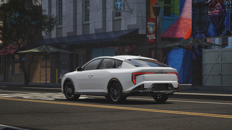 A white Kia K5 at a stop in a city environment