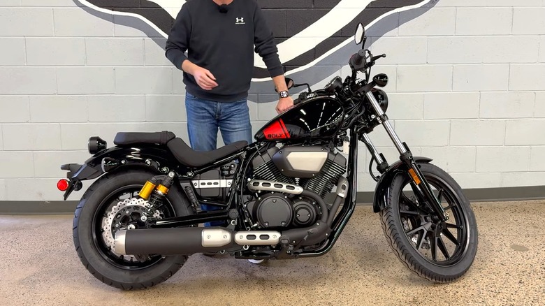 A black Yamaha Star Bolt R-Spec motorcycle positioned indoors with a person standing beside it, in front of a wall.