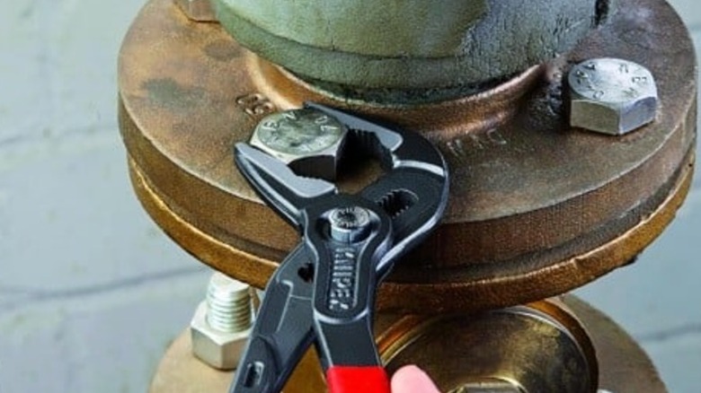 A close-up of Knipex adjustable pliers gripping a large bolt on a corroded industrial pipe flange.
