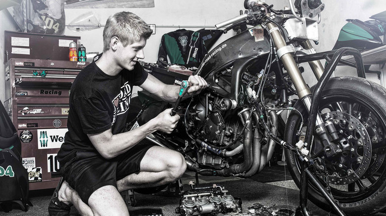 A mechanic kneeling in a workshop while working on a disassembled racing motorcycle, using Wera hand tools with turquoise accents.