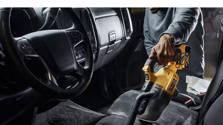A person using a yellow-and-black DeWalt cordless hand vacuum on a car's interiors.