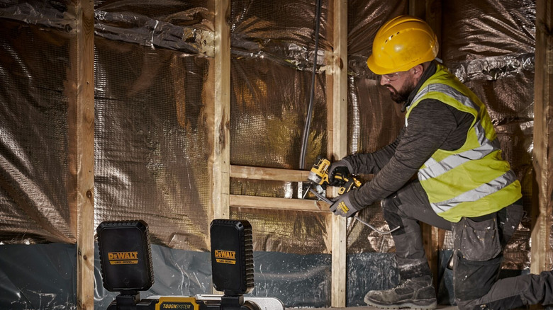 The DeWalt ToughSystem 2.0 Adjustable Work Light with Storage shining on a worker in a high-vis vest and helmet.