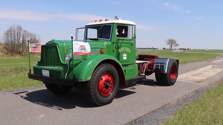A green Brockway classic truck making its way down a narrow road