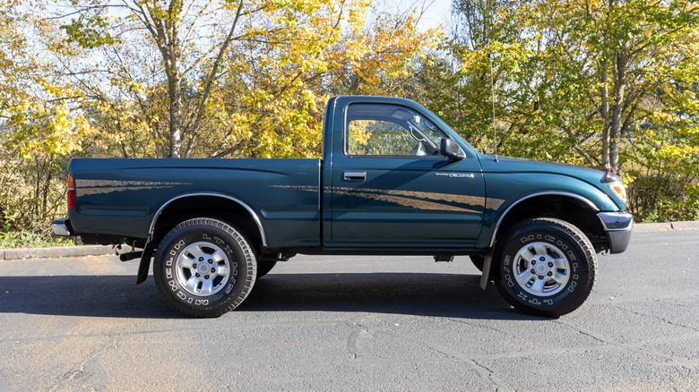 An old, dark green Toyota single cab pickup truck parked outside next to some trees
