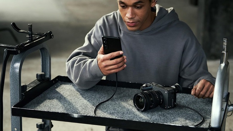 A person using a Sony FX2 camera connected to a phone