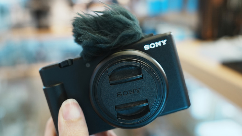 A person holding the Sony ZV-1F with a deadcat on the mic