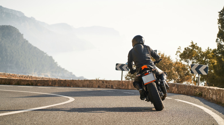 Back shot of man riding sport motorbike taking a curve surrounded by nature at mountain
