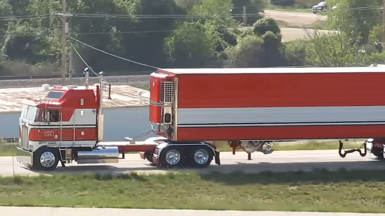 A vintage red and white cabover semi truck from BJ and the Bear, pulling a matching red trailer with white and black horizontal stripes.
