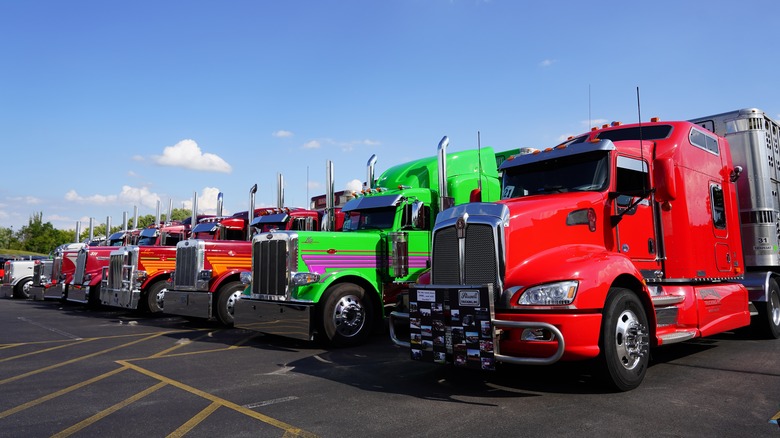 A lineup of brightly colored custom semi-trucks parked in a row under a clear blue sky