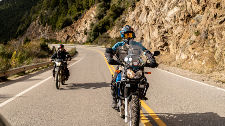 two motorcyclists riding windy road near cliffside