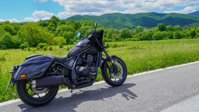 black 2021 Honda Rebel 1100 parked at the side of a road with greenery in the background