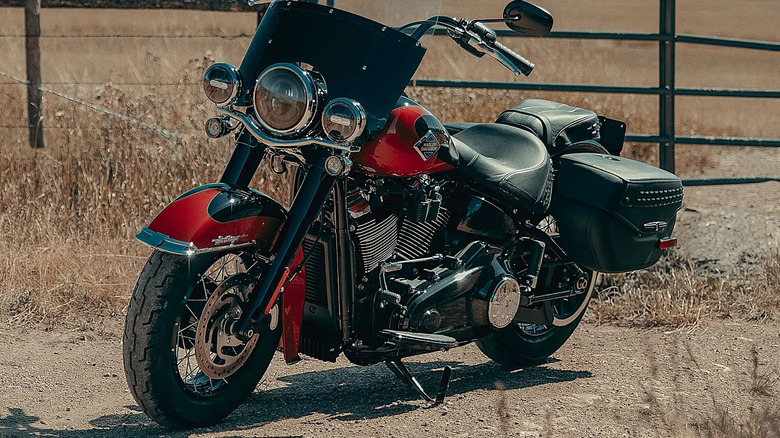 A gorgeous red 2025 Harley-Davidson Heritage Softail Classic motorcycle parked next to a fence