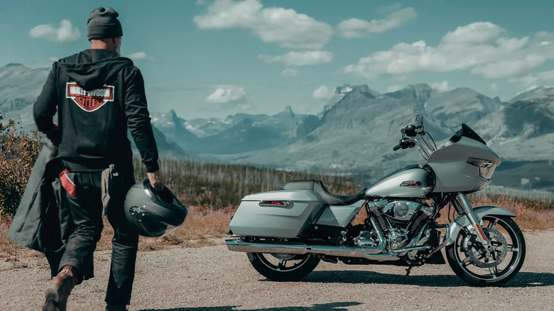 A man in Harley-Davidson clothing walking towards a silver 2025 Road Glide parked at the side of a road