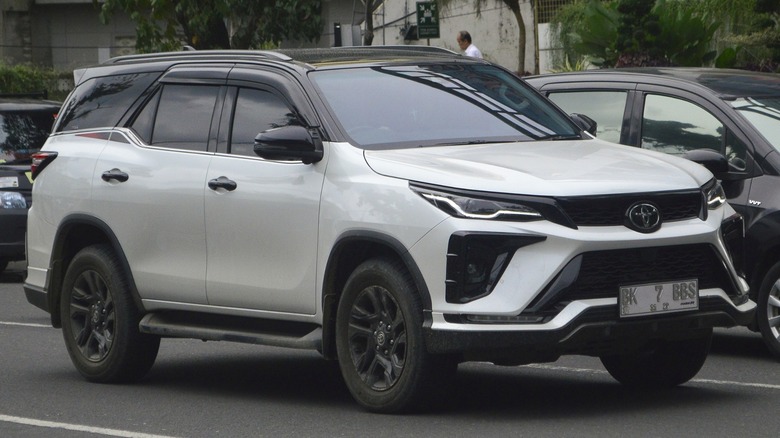 A white Toyota Fortuner in a parking lot, surrounded by a handful of other cars