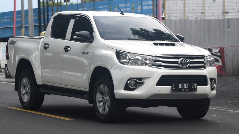 A white Toyota Hilux driving past some shipping tanks.