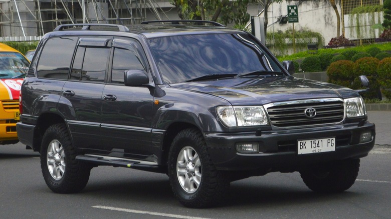 A Toyota Land Cruiser (J100) driving down a street with a partially constructed building in the background.