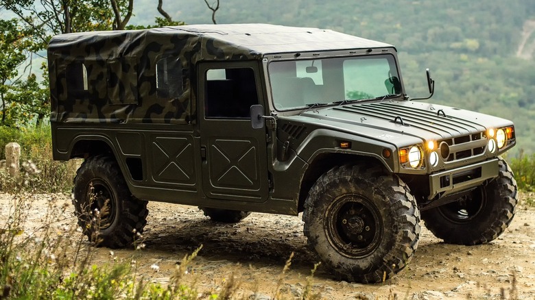 A camo-colored Toyota Mega Cruiser driving through a forest trail with dense greenery in the background
