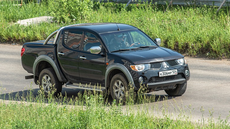 A Mitsubishi L200 pickup track trundling along a road bordered by grass