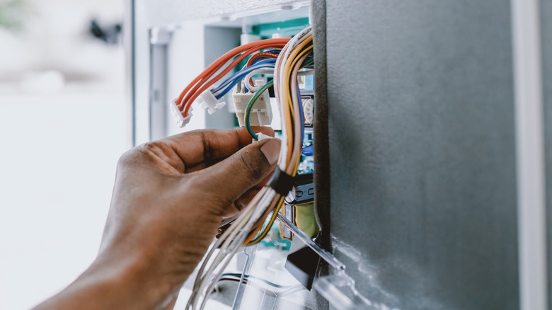 hand grabbing wires in a wall panel
