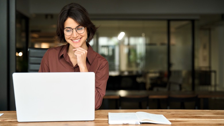 Woman with glasses looking at laptop screen while smiling
