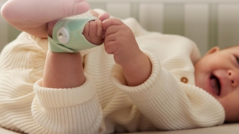 Baby in white outfit lying down holding foot with a green wrap