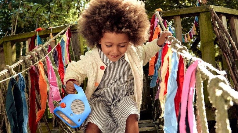 Child holding speaker while playing on a wooden treehouse