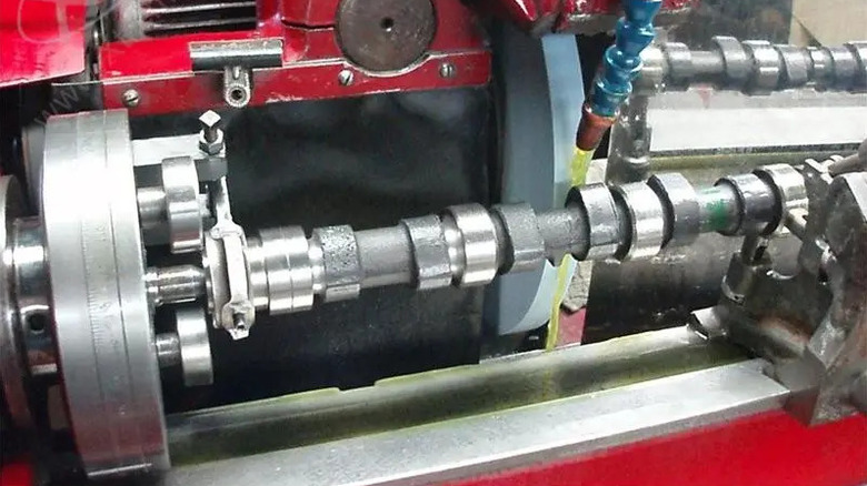 A Cummins camshaft being machined on a red industrial camshaft grinding machine.