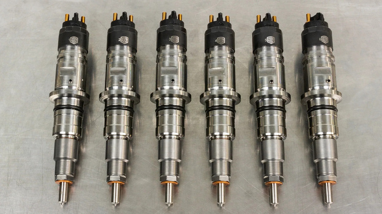 Six S&S Diesel Motorsport high-performance diesel fuel injectors neatly arranged on a metal surface.