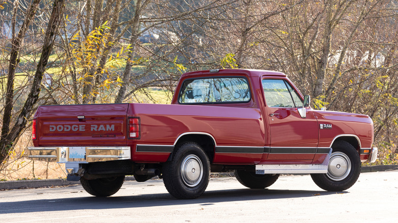 Rear and side view of a vintage red Dodge Ram pickup truck parked outdoors on a sunny day.