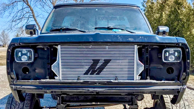 Front view of a lifted black pickup truck with no grille installed, showcasing a large Mishimoto intercooler.