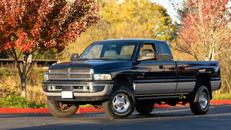 A black and silver Dodge Ram 2500 pickup truck parked on a sunny autumn day, with colorful red and yellow trees in the background.
