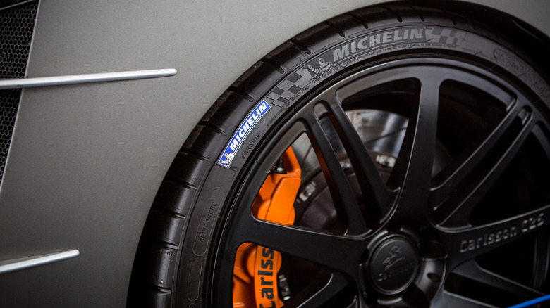A close up of a Michelin tire on a dark gray car with bright orange brake calipers