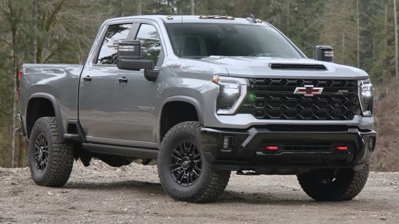 A gray Chevrolet Silverado 2500HD pickup truck is parked on a dirt clearing surrounded by trees.
